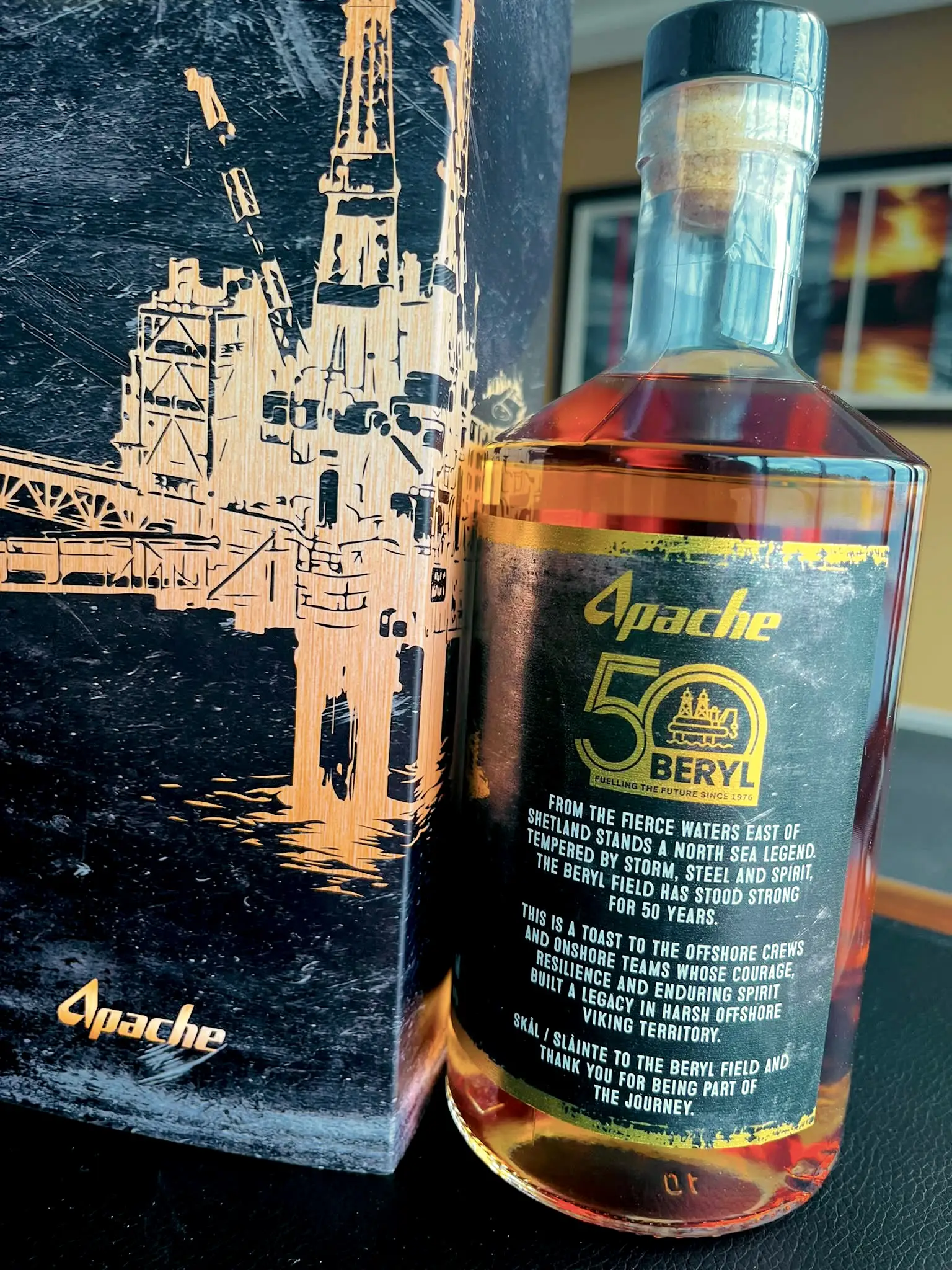 A bottle of Twice Buried Spiced Botanical Rum beside its bespoke Apache gift box, marking 50 years of the Beryl Field