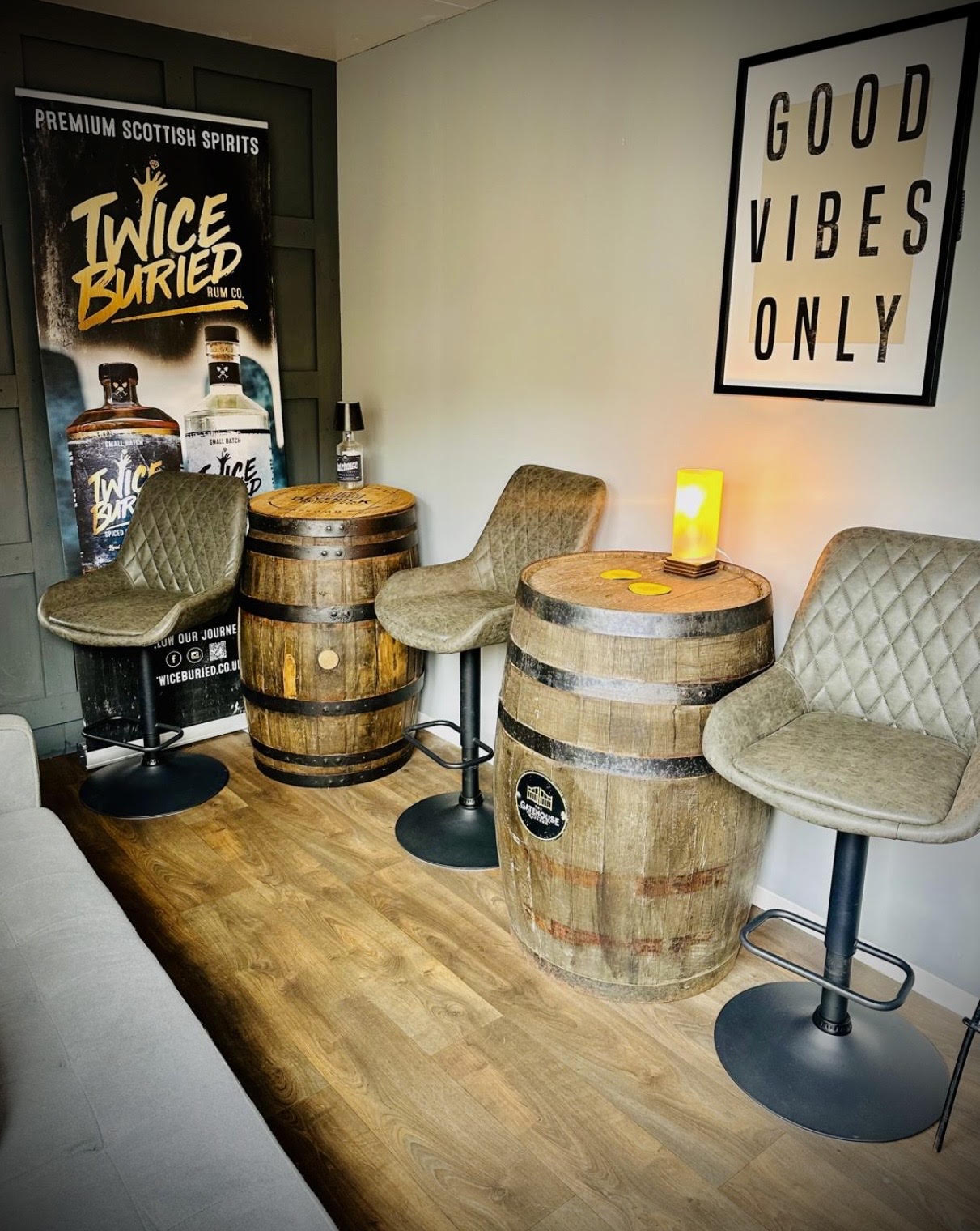 Barrel tables and stools beneath Twice Buried and Good Vibes Only signage