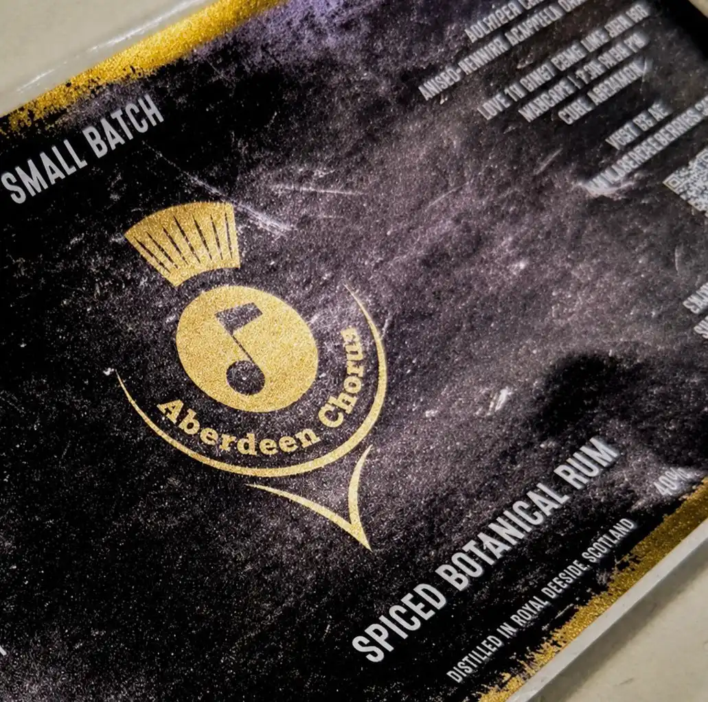A close-up of the bespoke Aberdeen Chorus label, with the choir's gold logo and QR code on a bottle of Spiced Botanical Rum